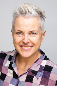 Picture of a smiling woman with short grey hair and a checked shirt